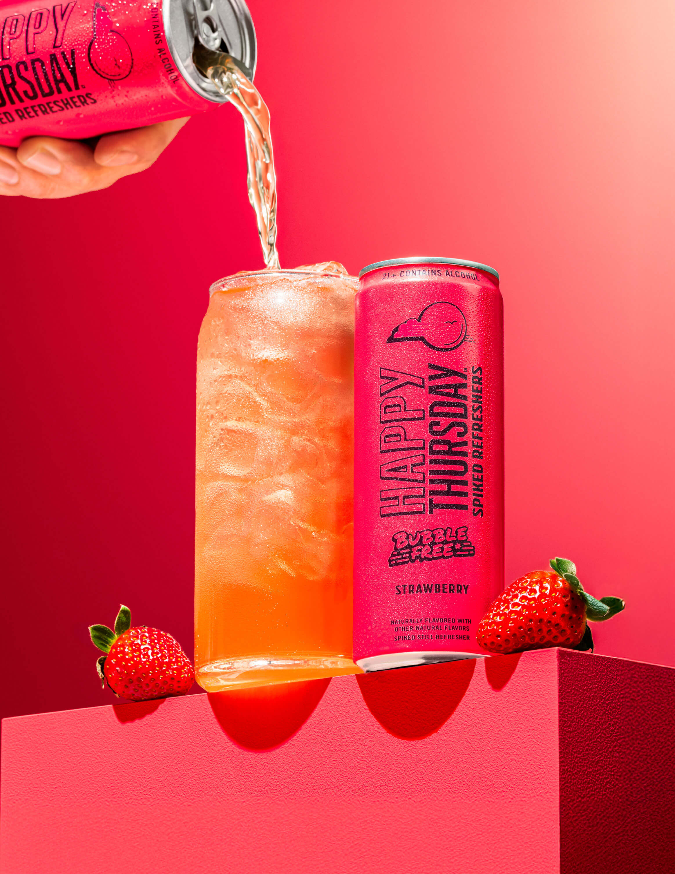 A can of Happy Thursday Strawberry Refresher is poured over ice into a glass, with Strawberry on a pink background